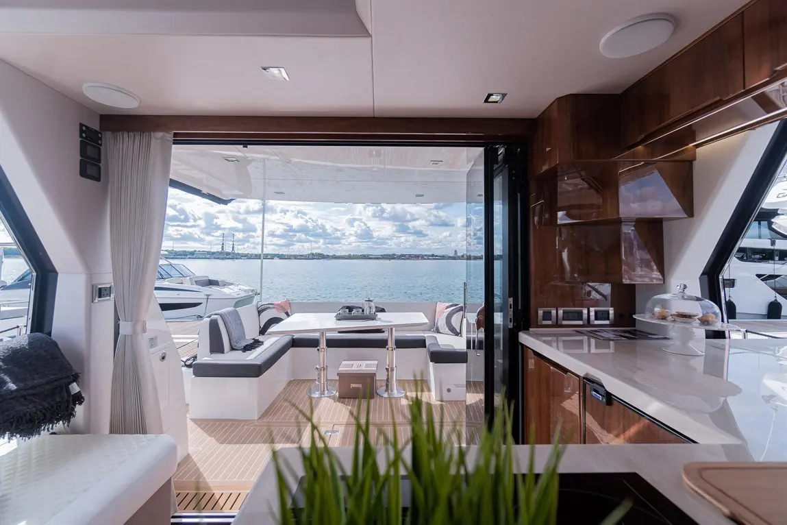 Luxurious yacht interior with a panoramic view of water, dining space, and modern kitchen features. Soft furnishings enhance comfort.
